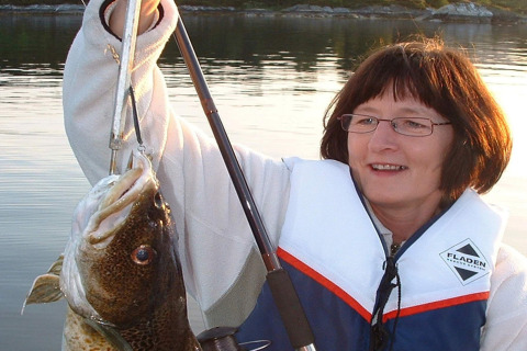Woman on houseboat '38507-SJØSTJERNEN' in Denmark proudly holding a large fish while wearing a life vest.