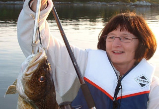 Woman on houseboat '38507-SJØSTJERNEN' in Denmark proudly holding a large fish while wearing a life vest.
