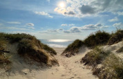 Blick durch Sanddünen auf das Meer bei Ulfborg, Dänemark, unter blauem Himmel mit Sonne.