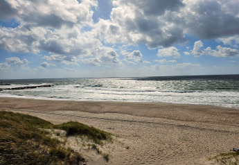 Foto af en sandstrand og hav med bølger fra feriehus til 8 personer i Ulfborg, Danmark, under dramatiske skyer.