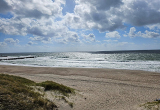 Foto af en sandstrand og hav med bølger fra feriehus til 8 personer i Ulfborg, Danmark, under dramatiske skyer.