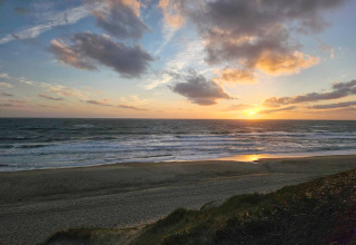 Solnedgang over havet set fra stranden ved et sommerhus i Ulfborg, Danmark, med skyer og rolige bølger.