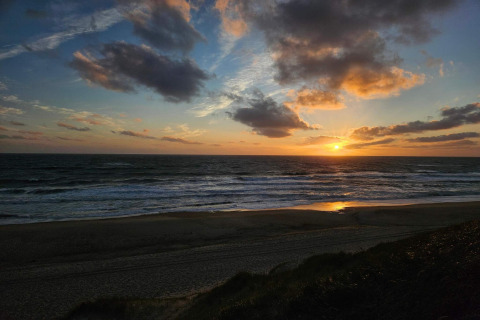 Sonnenuntergang am Meer, gesehen vom Strand nahe einem Ferienhaus in Ulfborg, Dänemark, mit Wolken.
