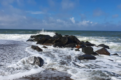Le onde si infrangono contro le rocce vicino a una casa vacanze a Ulfborg, Danimarca, cielo azzurro sopra.