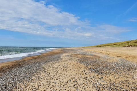Plage de galets et de sable près du chalet 8 personnes à Ulfborg, au Danemark, sous un ciel bleu.