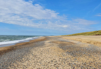 Plage de galets et de sable près du chalet 8 personnes à Ulfborg, au Danemark, sous un ciel bleu.