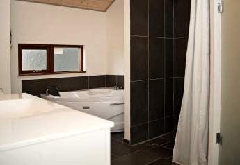 Salle de bain moderne avec baignoire d’angle, douche carrelée sombre et fenêtre à Ulfborg, Danemark.