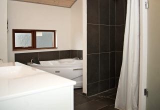 Salle de bain moderne avec baignoire d’angle, douche carrelée sombre et fenêtre à Ulfborg, Danemark.