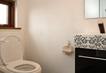 Badeværelse med åben toilet, papirholder og moderne vask på 8-personers feriehus i Ulfborg, Danmark.