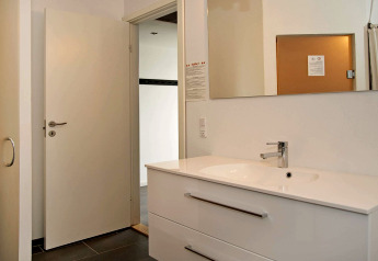 Salle de bain moderne avec lavabo blanc, miroir et porte ouverte dans un chalet 8 personnes à Ulfborg, Danemark.