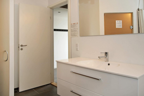Moderne badkamer met witte lavabo, spiegel en open deur in 8-persoons vakantiehuis te Ulfborg, Denemarken.