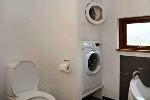 Et badeværelse i et sommerhus med toilet, vaskemaskine, tørretumbler og et vindue i Ulfborg, Danmark.