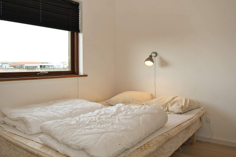 Schlafzimmer mit Doppelbett, zwei Kissen, Leselampe und großem Fenster im Ferienhaus in Ulfborg, Dänemark.
