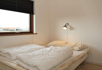 Slaapkamer met dubbelbed, twee kussens, leeslamp en groot venster in een vakantiehuis in Ulfborg, Denemarken.
