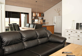 Moderne opholdsstue og køkken i feriehus i Ulfborg, Danmark, med sort lædersofa og spisebord til otte.
