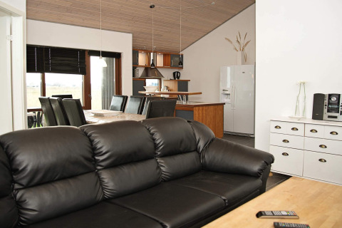 Moderne woon- en eetkamer in een vakantiehuis in Ulfborg, Denemarken, met zwarte lederen zetel en eethoek.
