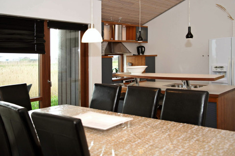 Spisestue og køkken i et moderne sommerhus i Ulfborg, Danmark, med lækre sorte læderstole og store vinduer.