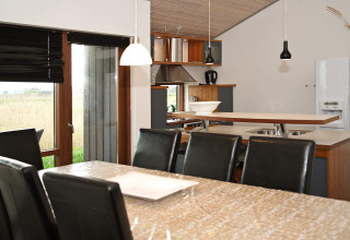 Essbereich und Küche in einem modernen Ferienhaus in Ulfborg, Dänemark, mit schwarzen Stühlen und Ausblick.