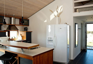 Moderne Küche eines Chalets in Ulfborg, Dänemark, mit weißem Kühlschrank, Frühstücksbar und Holzdecke.