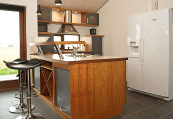Cucina moderna in una casa vacanze a Ulfborg, Danimarca, con isola, sgabelli e frigorifero grande.