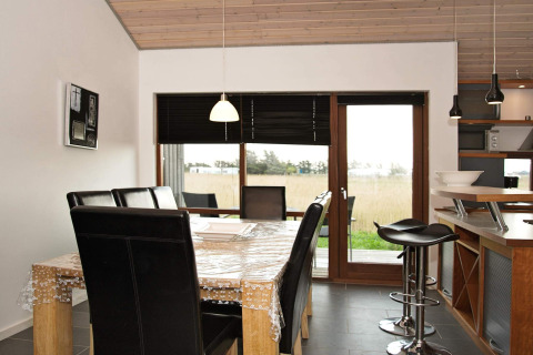 Eetruimte met houten tafel, lederen stoelen en uitzicht buiten in een vakantiewoning in Ulfborg.