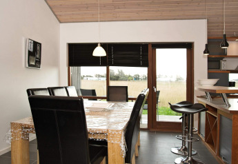 Eetruimte met houten tafel, lederen stoelen en uitzicht buiten in een vakantiewoning in Ulfborg.