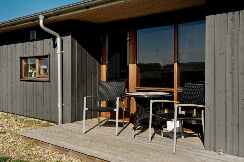 Piccola terrazza in legno con due sedie e un tavolo davanti a uno chalet moderno a Ulfborg, Danimarca.