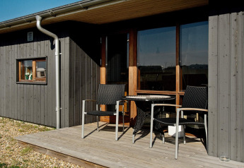 Piccola terrazza in legno con due sedie e un tavolo davanti a uno chalet moderno a Ulfborg, Danimarca.