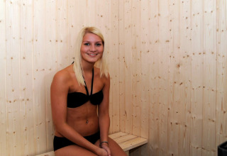 Giovane donna in bikini nero sorride seduta in una sauna di legno in casa vacanze per 8 persone a Ulfborg, Danimarca.