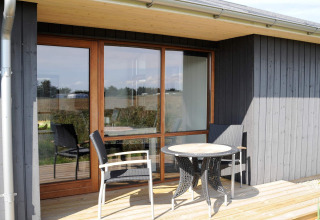 Buitenterras aan 8-persoons vakantieverblijf in Ulfborg, Denemarken, met tafel, stoelen en houtbekleding.