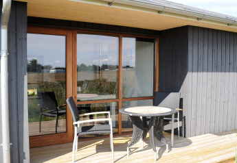 Terrazza esterna di casa vacanza per 8 persone a Ulfborg, Danimarca, con tavolo, sedie e rivestimento in legno.