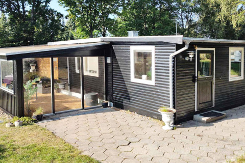 Exterior view of a black wooden holiday home with large windows and patio in Allingåbro, Denmark.