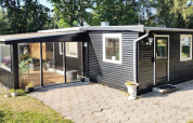 Außenansicht eines modernen, schwarzen Ferienhauses mit Terrasse und Wintergarten in Allingåbro, Dänemark.