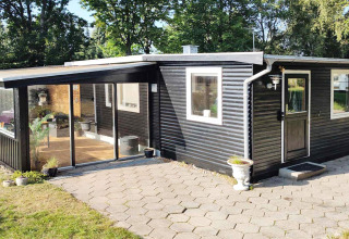 Buitenzicht op een zwart houten vakantiehuis met grote ramen en terras in Allingåbro, Denemarken.