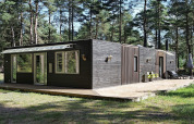 Modern zwart houten vakantiehuis in Hadsund, Denemarken, omgeven door bos, met terras en grote ramen.