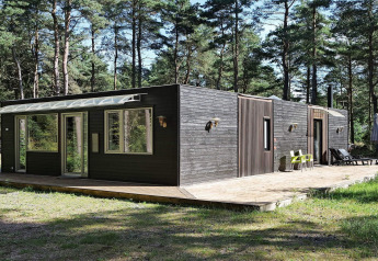 Moderne sort træferiebolig i Hadsund, Danmark, omgivet af skov, med terrasse og store vinduer.