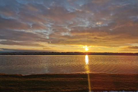 Tramonto sull'acqua calma vicino alla casa vacanze per 6 persone a Hadsund, Danimarca, cielo nuvoloso.