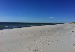 Playa de arena solitaria cerca de Hadsund, Dinamarca, con mar tranquilo y cielo azul despejado.