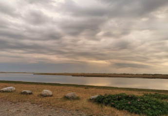 Vue paisible sur l’eau et la prairie sous un ciel nuageux près du gîte 6 personnes à Hadsund, au Danemark.
