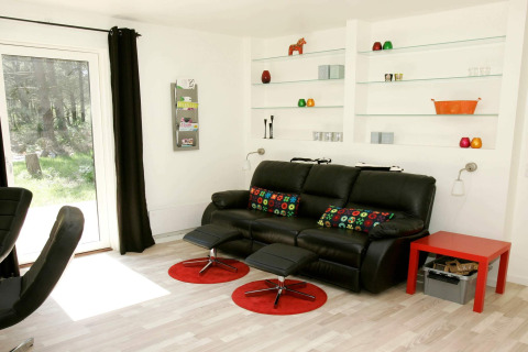 Salon moderne avec canapé noir, coussins colorés et étagères dans maison de vacances à Hadsund, Danemark.