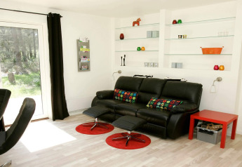 Modernes Wohnzimmer mit schwarzem Sofa, bunten Kissen und Regalen in einem Ferienhaus in Hadsund, Dänemark.