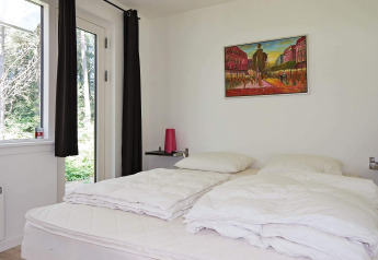 Lichte slaapkamer in vakantiehuis in Hadsund, Denemarken, met kunst aan de muur en uitzicht op de natuur.