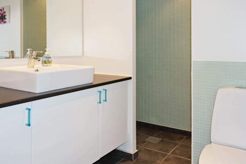 Moderne badkamer in een vakantiehuis in Hadsund, Denemarken met lavabo, spiegel, toilet en douche.