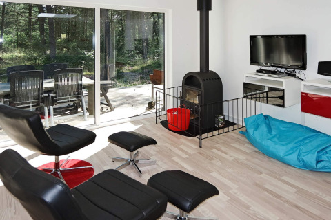 Modern living room with black chairs, wood stove, blue bean bag, and forest view at Hadsund holiday home.