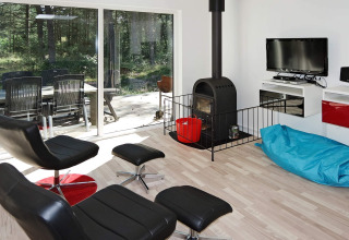 Moderne stue med sort lænestol, brændeovn, blå sækkestol og udsigt til træterrasse i Hadsund lodge.