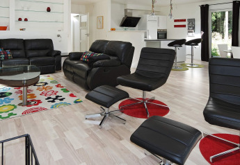 Modernes Wohnzimmer in einem Ferienhaus in Hadsund, Dänemark, mit Ledersofas, buntem Teppich und Küche.