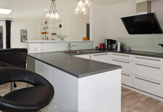 Cucina moderna con piano nero, mobili bianchi e lampade sospese in una casa vacanze a Hadsund, Danimarca.
