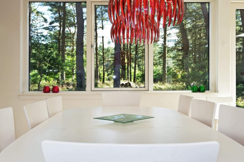 Salle à manger avec table blanche, lustre rouge moderne et grandes fenêtres donnant sur la forêt à Hadsund, Danemark.