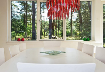 Salle à manger avec table blanche, lustre rouge moderne et grandes fenêtres donnant sur la forêt à Hadsund, Danemark.