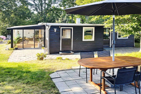 Außenbereich des 4-Personen-Ferienhauses in Allingåbro, Dänemark, mit Terrasse, Tisch und dunkler Fassade.